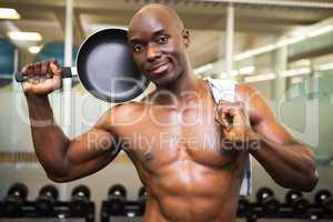 Shirtless muscular man holding frying pan in gym