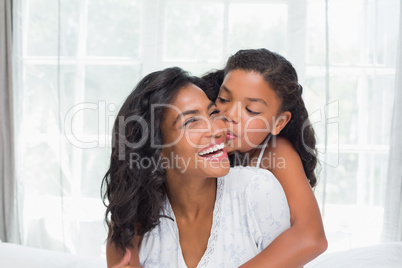 Smiling mother and daughter posing together on bed