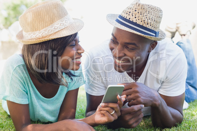 Happy couple lying in garden together looking at smartphone