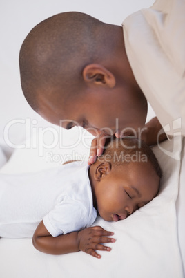 Baby boy sleeping peacefully on couch with father kissing head