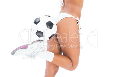 Fit girl in white bikini holding football at her foot