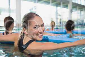 Happy fitness class doing aqua aerobics with foam rollers