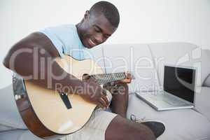 Casual man sitting on sofa playing the guitar with laptop