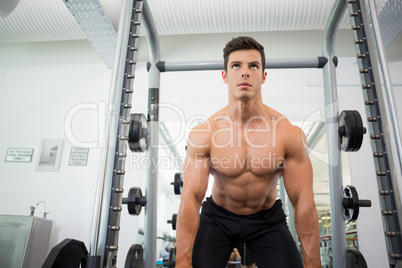 Shirtless muscular man lifting barbell in gym