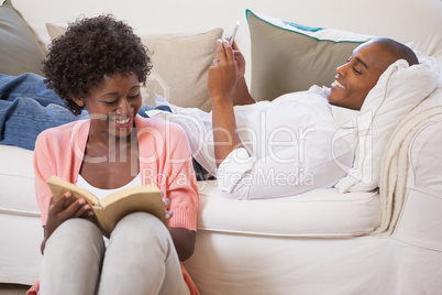 Happy couple relaxing together reading book and using smartphone