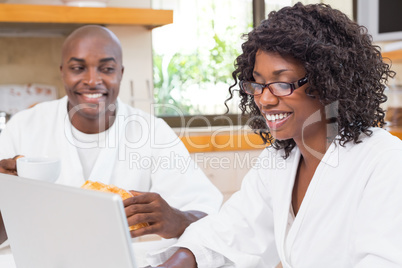 Happy couple having breakfast together at table using laptop