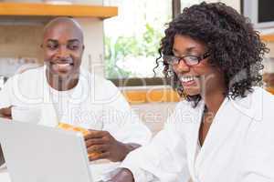 Happy couple having breakfast together at table using laptop