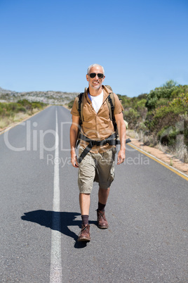 Handsome hiker walking on road and smiling at camera Handsome hiker walking on road and smiling at camera