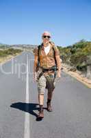 Handsome hiker walking on road and smiling at camera