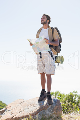 Handsome hiker holding map at mountain summit