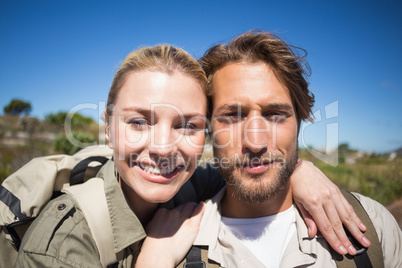 Happy hiking couple walking on mountain terrain smiling at camer