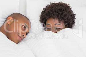 Happy couple lying in bed under the duvet