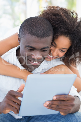 Attractive couple sitting on couch together looking at tablet