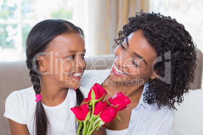 Pretty mother sitting on the couch with her daughter holding ros