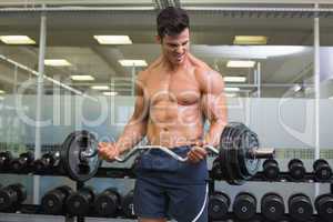 Shirtless muscular man lifting barbell in gym