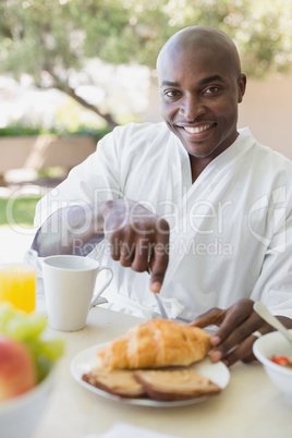 Handsome man in bathrobe having breakfast outside