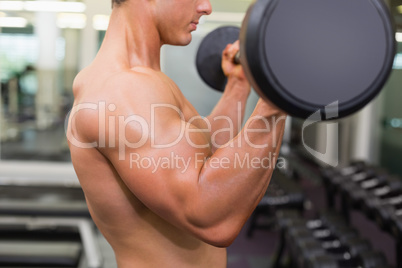 Mid section of a shirtless muscular man lifting barbell