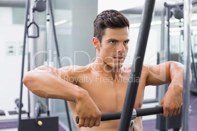 Shirtless muscular man using biceps pull up in gym
