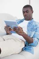 Casual man lying on sofa using his tablet pc