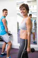 Fit couple lifting weights together smiling at camera