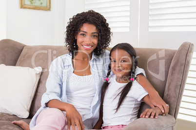 Pretty mother sitting on the couch with her daughter smiling at