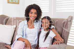 Pretty mother sitting on the couch with her daughter smiling at