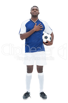 Football player in blue standing with the ball listening to anth