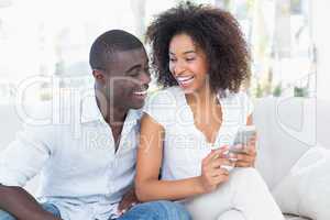 Attractive couple sitting on couch together looking at smartphon
