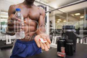Shirtless muscular man holding vitamin pills