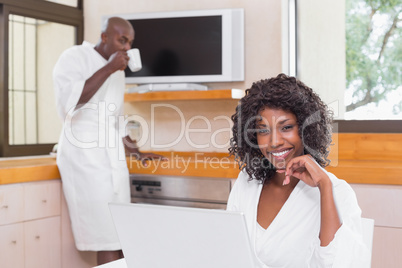 Pretty woman in bathrobe using laptop at table with partner in b