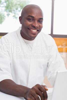 Happy man in bathrobe using laptop at table