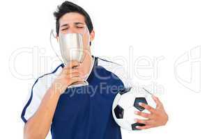 Football player in blue holding winners cup and ball