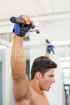 Side view of a shirtless male body builder doing pull ups