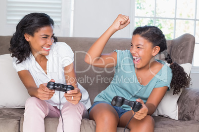 Happy mother and daughter playing video games together on sofa
