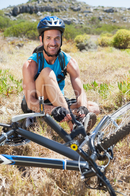 Fit cyclist tying his shoelace on mountain trail smiling at came