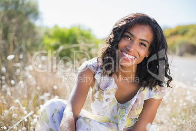 Happy pretty woman sitting on the grass in floral dress