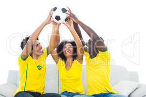 Happy football fans in yellow sitting on couch with ball
