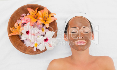 Smiling brunette getting a mud treatment facial beside bowl of f