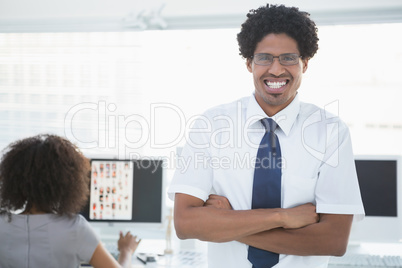 Young handsome editor smiling at camera with colleague working b