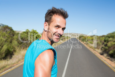 Fit man jogging on the open road smiling at camera