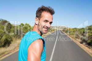 Fit man jogging on the open road smiling at camera