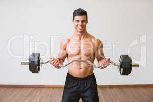 Shirtless muscular man lifting barbell in gym