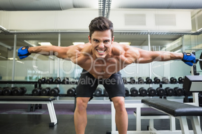 Smiling shirtless bodybuilder with arms outstretched in gym