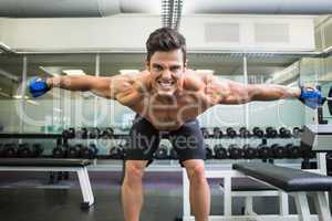 Smiling shirtless bodybuilder with arms outstretched in gym