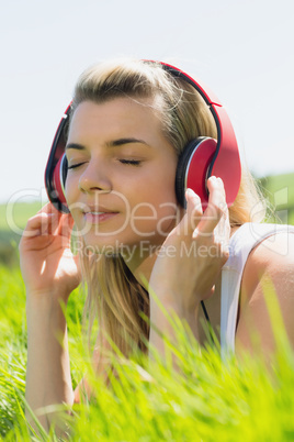 Pretty blonde lying on grass listening to music