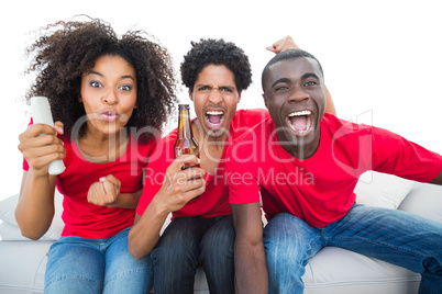 Football fans in red cheering on the sofa with beers