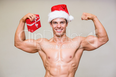Portrait of shirtless macho man in santa hat holding gift