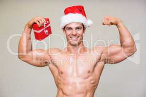 Portrait of shirtless macho man in santa hat holding gift