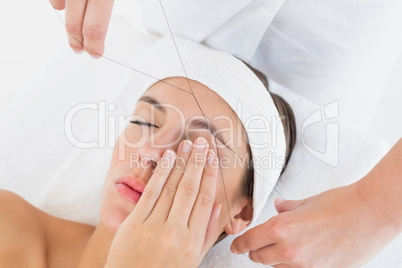 Hands threading beautiful womans eyebrow