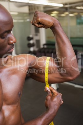 Muscular man measuring biceps in gym